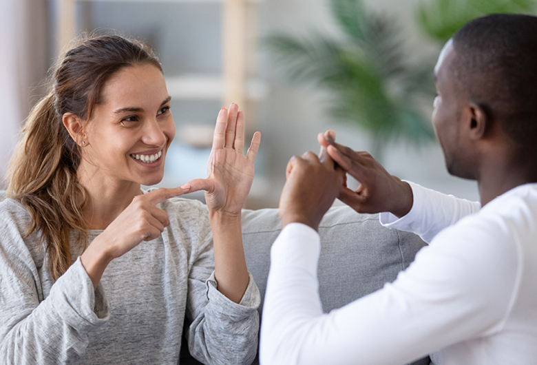 A smiling woman and a man sitting opposite each other on a sofa, communicating using sign language.