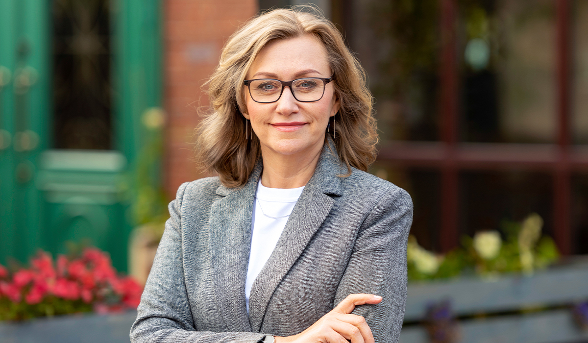 A businesswoman in a gray blazer stands outside a storefront with a confident expression