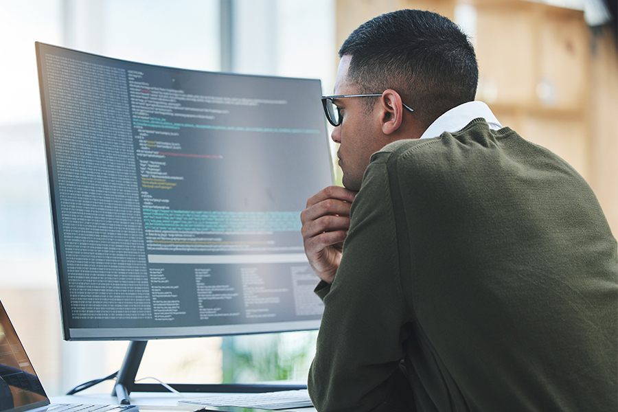 IT professional analyzing code on a large desktop monitor in an office setting