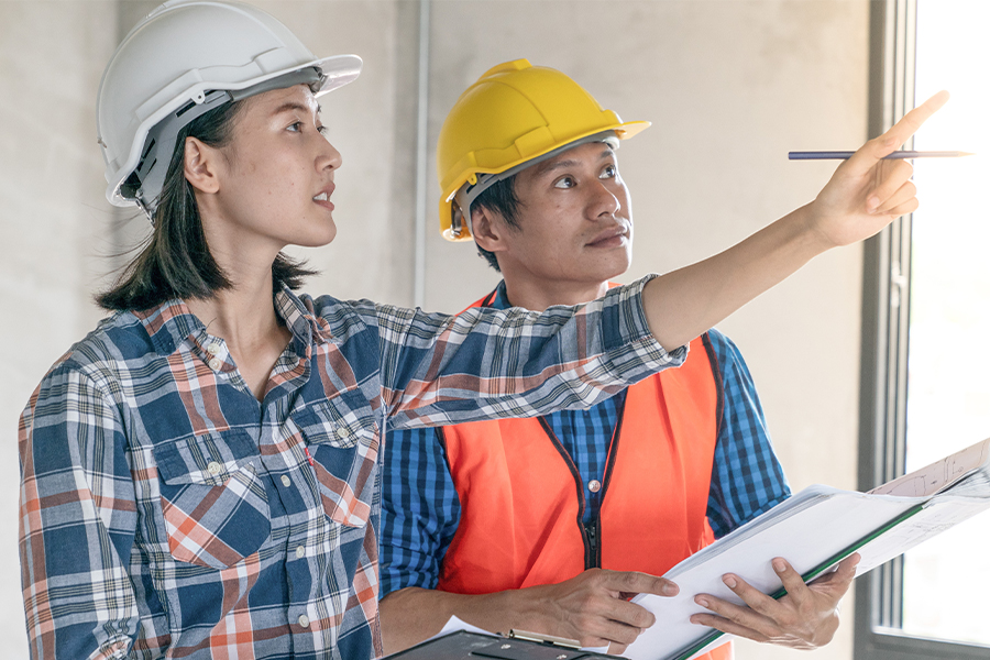 Two construction professionals in hard hats reviewing architectural plans at a job site.