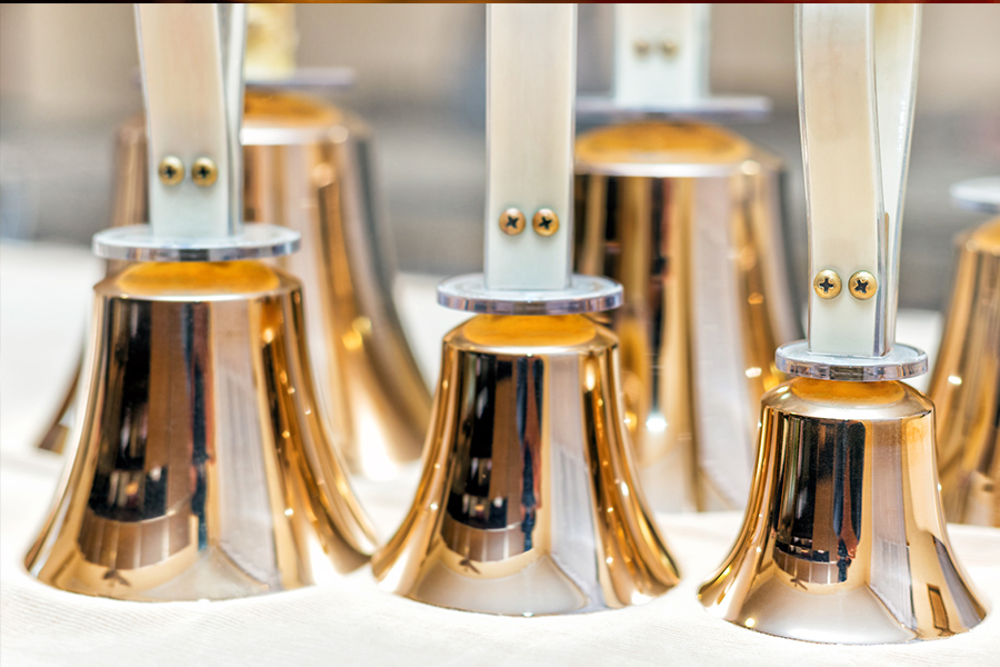 Close-up of gold handbells arranged in a row on a white surface.