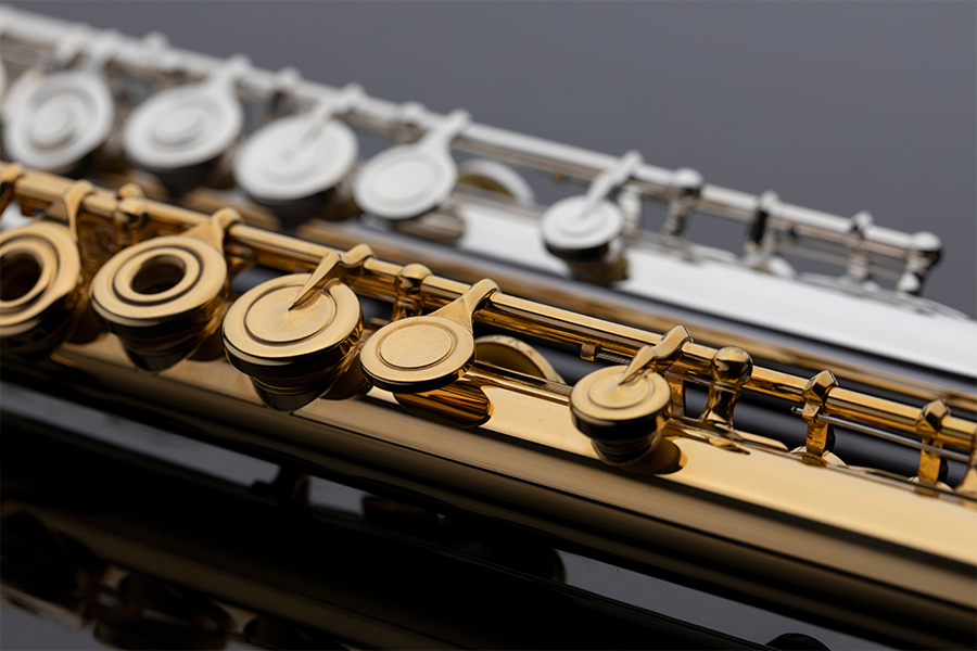 Close-up of gold and silver flute keys overlapping against a dark background.
