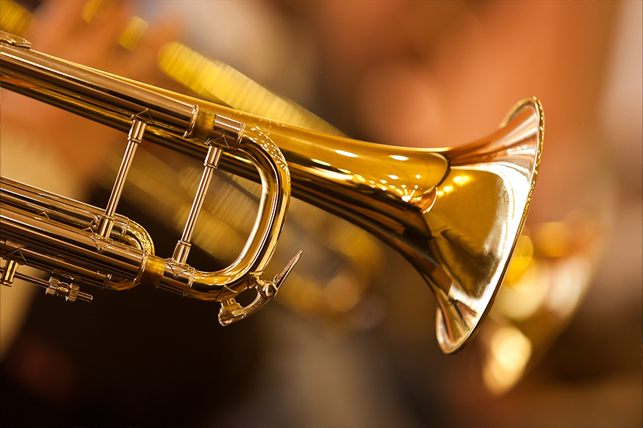 Close-up of a trumpet bell with a blurred band performing in the background.