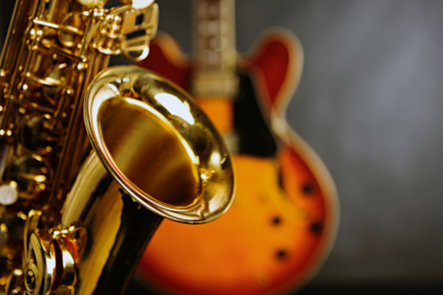 Close-up of a saxophone bell with an electric guitar blurred in the background.