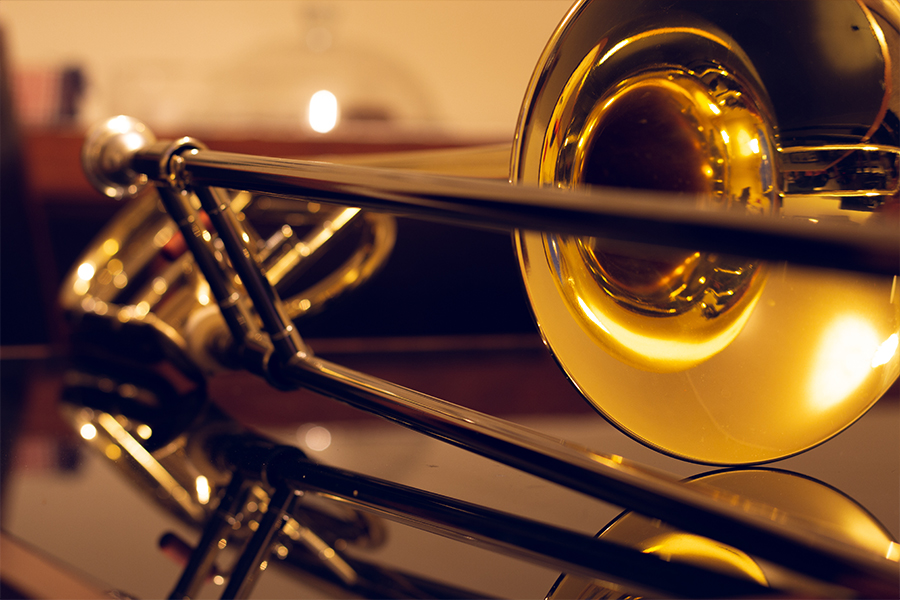 Close-up of a trombone bell reflecting warm light against a dark background.