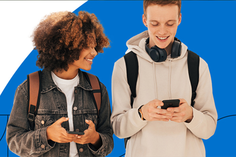 Two students stand with cell phones, looking at an app on their phone. 