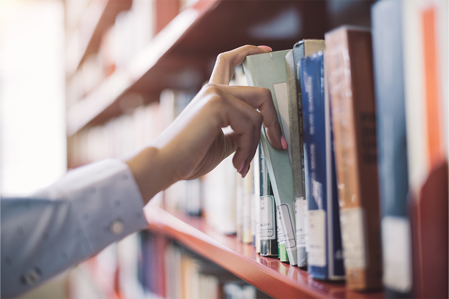 A close-up shot of a hand pulling a book from a wooden bookshelf, with a blurred background.