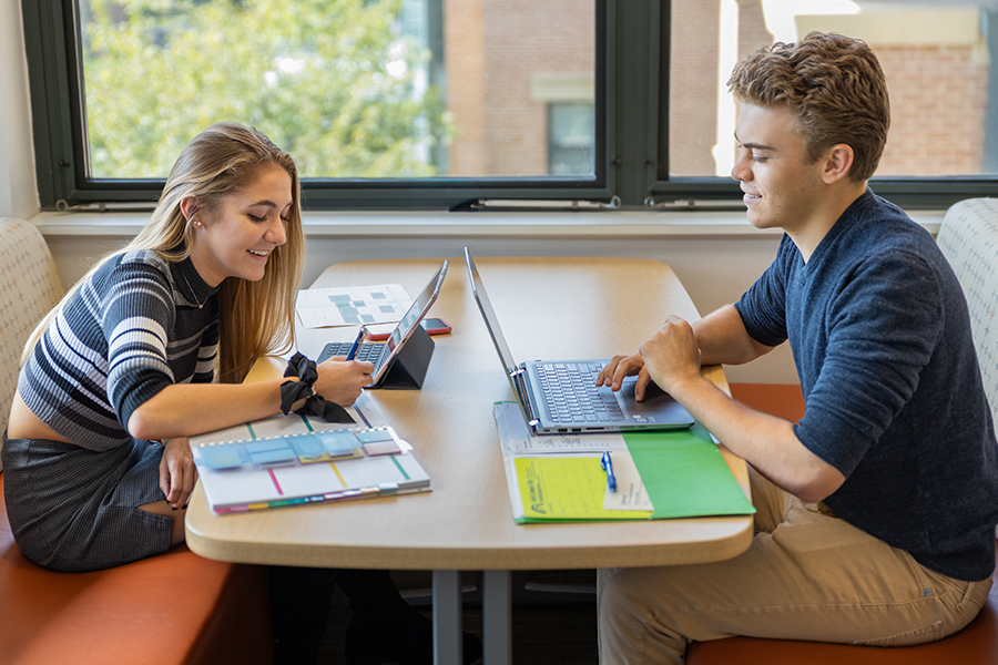 male and female students sitting at table with laptops