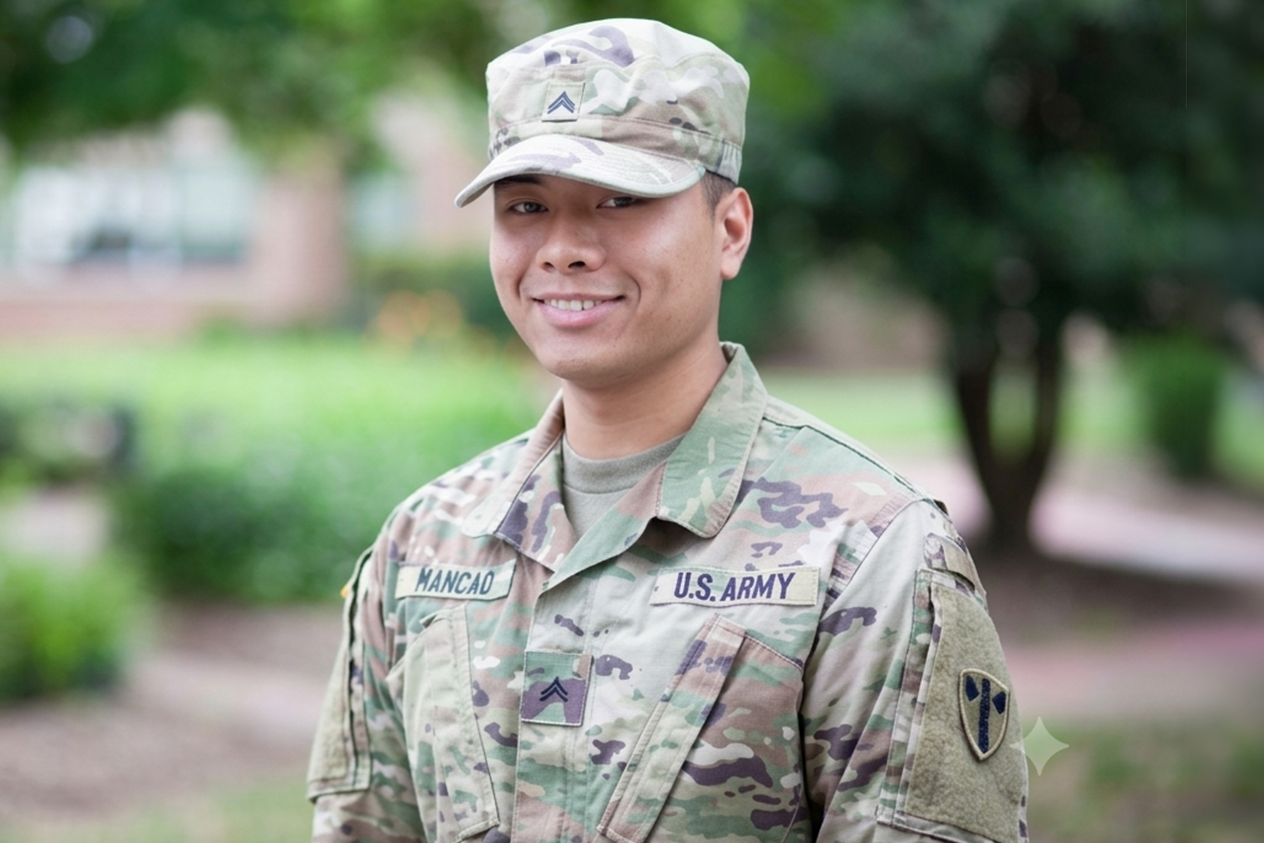 A smiling U.S. Army soldier in camouflage uniform and cap stands outdoors on a green campus.