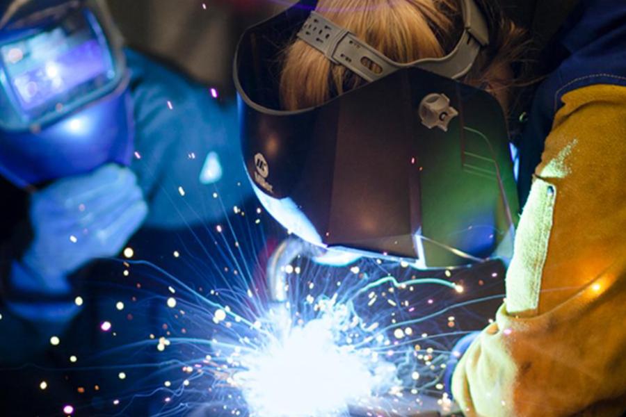 Two welders in protective helmets and gloves work together as bright sparks fly from a weld point.