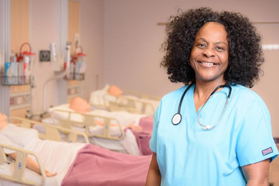 FCC CNA student in blue scrubs and stethoscope smiling in the Health Sciences simulation lab