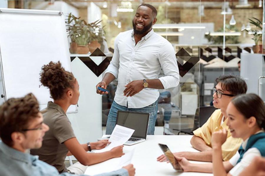 A smiling professional leading a presentation or workshop for a group of colleagues in a modern office.