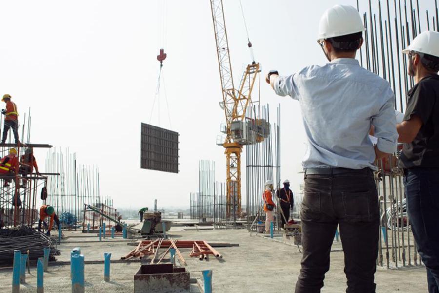 Construction site engineers in hard hats supervising a crane lifting materials at a high-rise project.