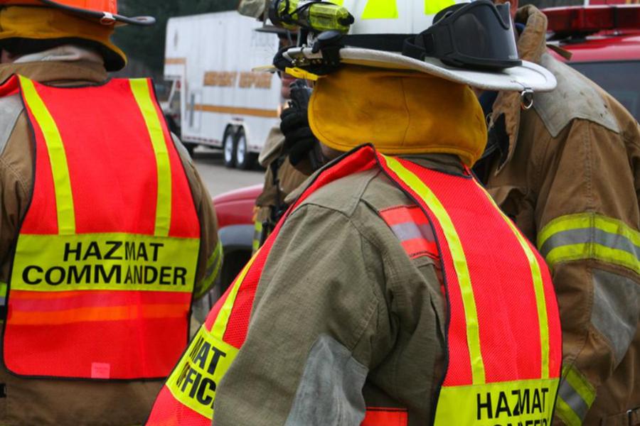 First responders in full protective gear and high-visibility vests labeled "Hazmat Commander."