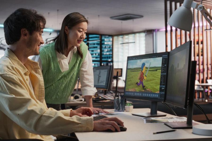 Two colleagues in a modern studio collaborate on a computer to design an animated character for a video game.