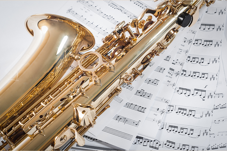 Close-up of a gold saxophone lying across sheets of printed music.