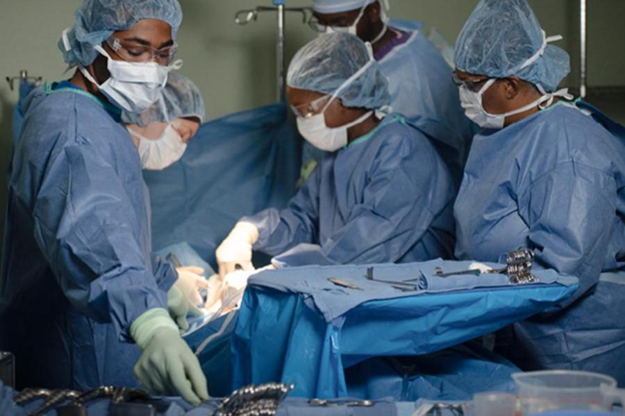 A surgical team in full blue sterile scrubs, masks, and caps performs a procedure in a modern operating room, focusing on precision and teamwork.