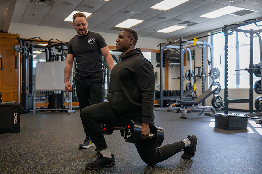 A student in a sports science lab monitors data on a computer while an athlete wearing a VO2 max respiratory mask runs on a treadmill.
