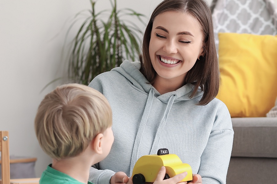 A smiling young woman plays with a toddler on the floor of a living room