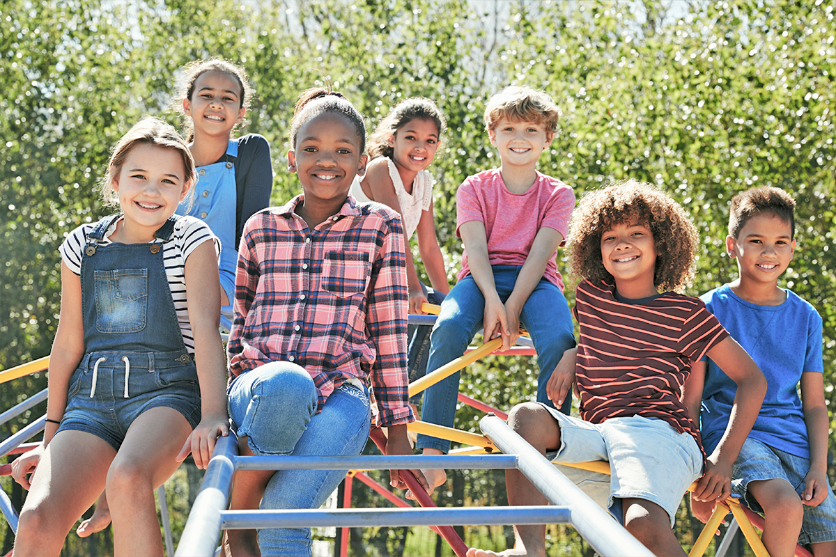 A group of children smile together outdoors on a sunny day at FCC