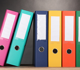 A row of vibrant, multi-colored office binders with blank white spine labels on a shelf.