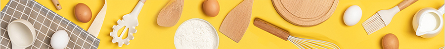 Baking ingredients and wooden kitchen tools arranged on a bright yellow background, including eggs, a bowl of flour, a whisk, spatula, spoon, cutting board, pastry cutter, and a small pitcher.