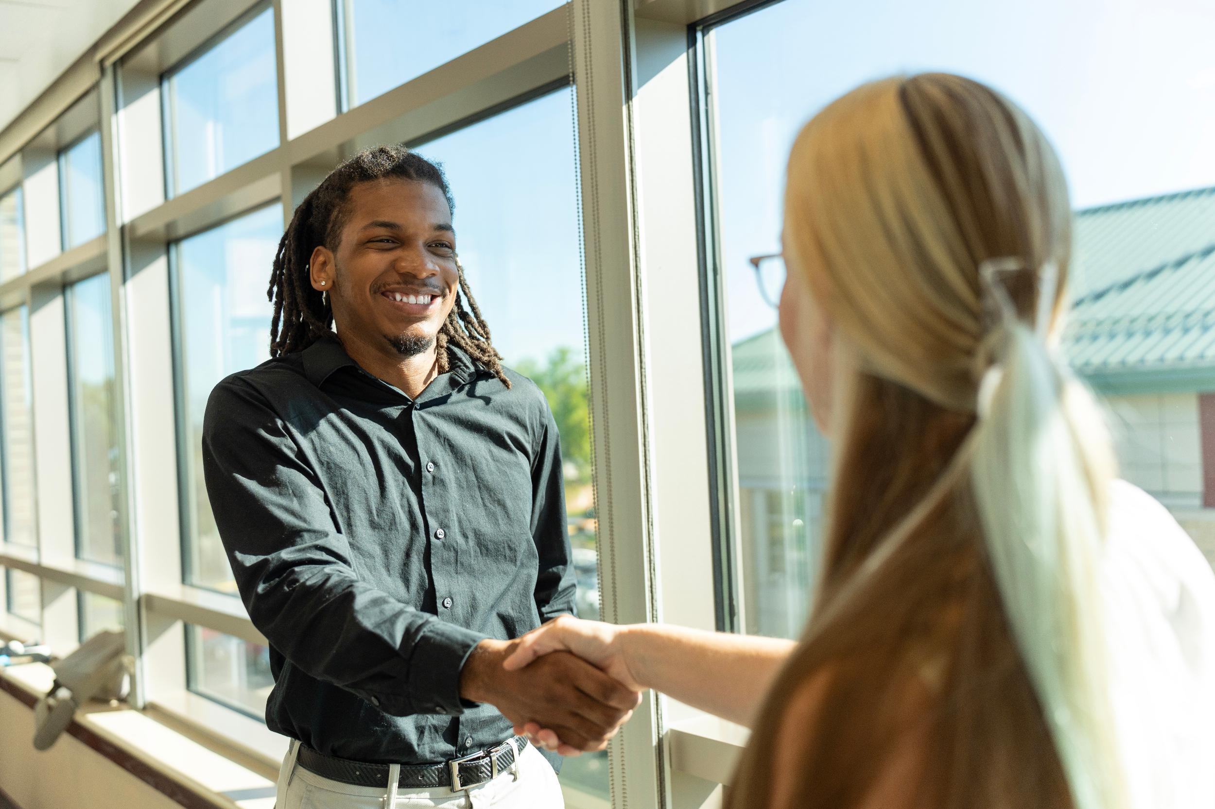 man in dark shirt shaking hands with woman with blond hair